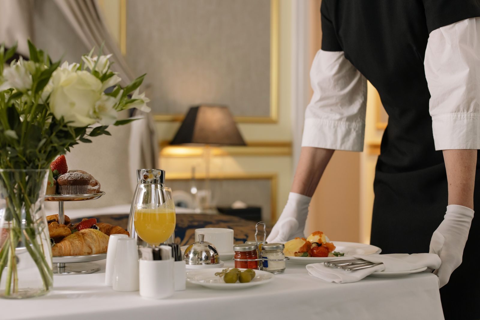 Breakfast tray with croissants and juice being set out by a server in white gloves