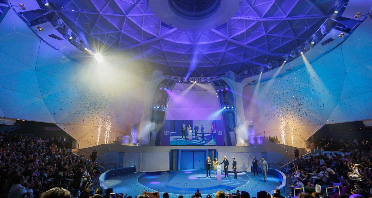Audience watching a stage show under blue lights in a large cruise ship theater